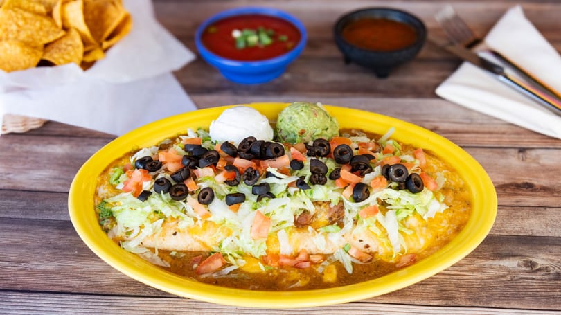 A large burrito covered in lettuce, tomatoes, black olives, sour cream, and guacamole.