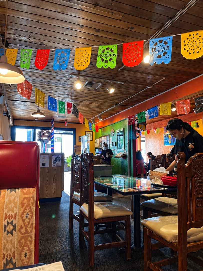 A vibrant Mexican restaurant interior with colorful papel picado banners, wooden tables, and a server.