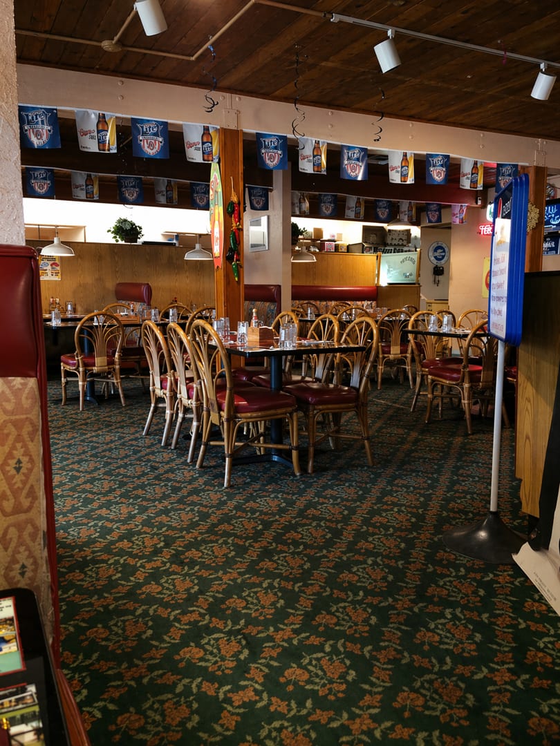 Empty restaurant dining room with wooden tables, red chairs, and beer banners hanging from the ceiling.