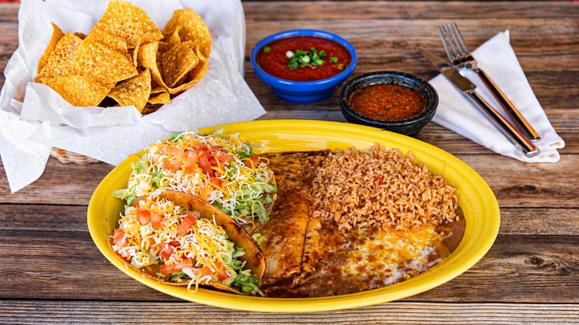 A vibrant Mexican combo platter with tacos, enchiladas, rice, beans, chips, and salsa on a wooden table.
